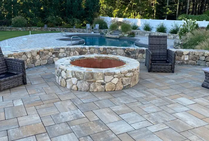 Stone firepit and paver patio beside a pool